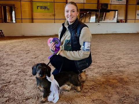 Kvinna sitter med hund på huk med priser i handen